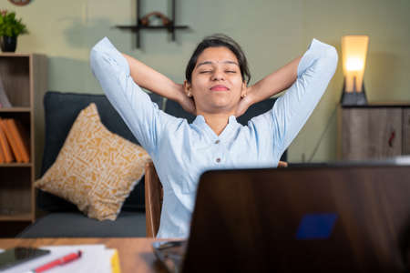 young business woman feeling relief after completion of work by holding hands behind head with smile...
