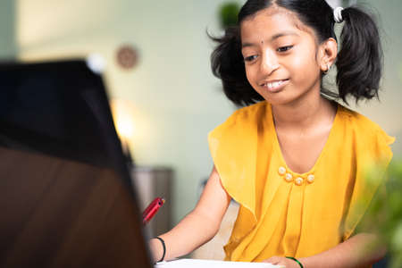 Concept of homeschooling, online education or e-learning, young girl busy in writing by looking into...