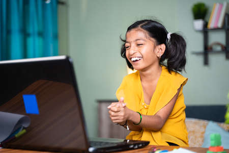 happy disabled Young girl kid laughing and clapping by looking fun online videos on laptop at home - concept of kids having fun during leisure timeの写真素材