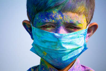 Young boy with medical face mask played holi during festival of colours and looking into camera - concept of holi celebration during  pandemicの写真素材