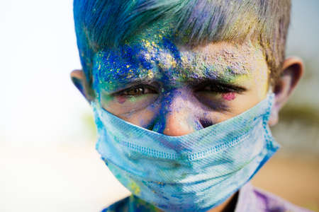Head Shot of Young boy with medical face mask played holi the festival of colours and looking into...