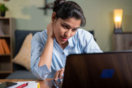 Young business woman suffering from neck pain while busy working on laptop - concept of over work, strain, stressed out, uncomfortable position or posture.の写真素材