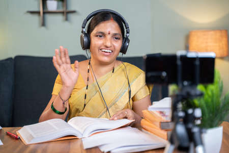 Indian woman greeting students in front of mobile during virtual online class at home - concept of new normal education, e-teaching, technology .の写真素材