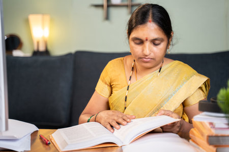 Indian woman busy preparing form fom seeing books for teaching online class - 40s lady studying by referring books for examination at home.の写真素材