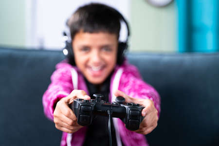 Close up selective focus on joystick, kid enjoying videogame using gamepad at home while sitting on sofaの写真素材