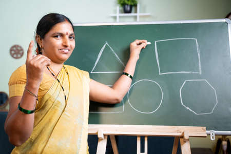 Indian woman busy explaining from board during online class by looking camera at home - Concept of...