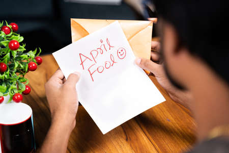 Shoulder shot of young man receiving prank latter - Concept of April fools day prank showing by sending surprise letter, after opening mentioned april fool in the latter.の写真素材