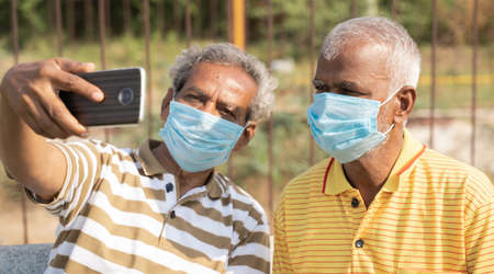 elderly friends with medical face mask taking selfie while sitting at park