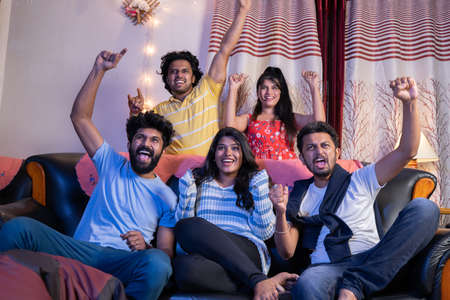 Group of Indian cricket fans shouting and cheering up to support the team while watching sports on tv at homeの写真素材