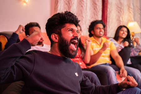 Group of young fans cheering and shouting for their team support while waching sports on tv from homeの写真素材