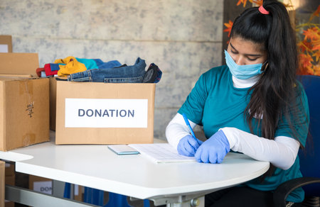 Young girl volunteer with medical face mask and gloves with clipboard Noting down donors information...