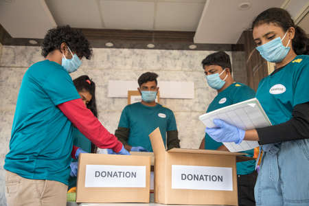 Focus on front girl, Group of volunteers busy working by arranging clothes and donation boxes during...
