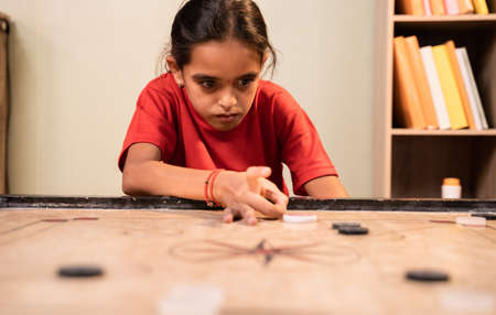 Front view of alone Young girl kid practicing or playing Carrom board at home - Concept of autism and introvert.の写真素材