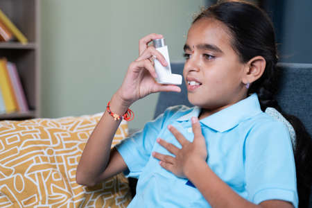 Young girl rubbing her chest after taking asthmatic inhaler at home - Concept of Teenager kids healthcare and medical.の写真素材