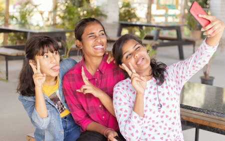 Focus on last girl, Young teenager girls with grimacing taking selfie at restaurant - girls having fun by taking photos on mobile phone - Concept best friends and youth culture.の写真素材