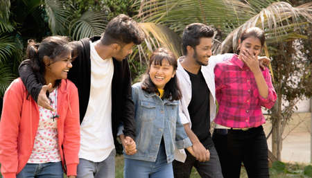 Group of five happy young friends laughing while walking by holding hands - concept of having fun,...
