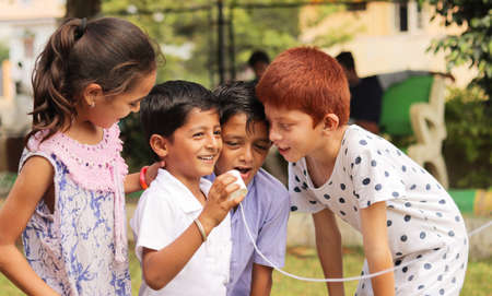 group of children having fun by playing with String Telephone during holiday summer camp - Concept of brain development and socializing by playing outdoor games in the technology driven world.の写真素材