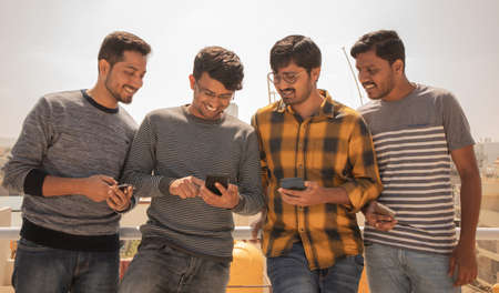 Group of young people watching mobile phone on terrace and laughing - friends using mobile phone...