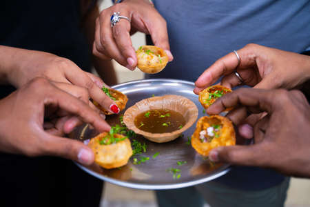 Close up, group of friends Hands taking pani puri Snacks from the plate - Concept of Sharing food or...