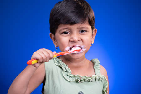 Portrait of girl kid brushing teeth on blue color background - concept of child healthy tooth by...