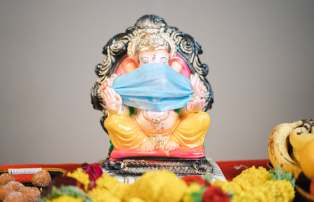 Ganesha or ganapati idol with medical face mask kept for festival celebrations during coronavirus covid pandemic to encourage people to wear mask.の写真素材