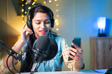 Young Indian girl vlogger live recording or streaming and checking likes, comments or chatting on social media with channel subscribersの写真素材