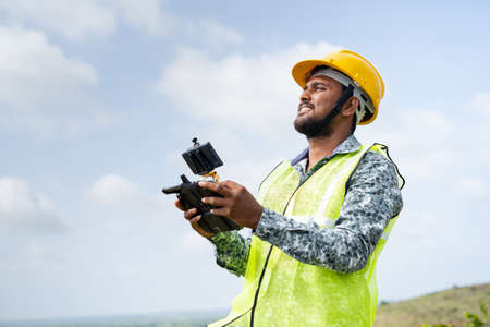 Drone pilot with safety helmet operating drone using remote controller - concept of engineer using drone technology to survey landの写真素材