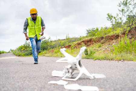 Worried drone operator running in hurry near crashed drone on road - concept of UAV damage or accident while flyingの写真素材