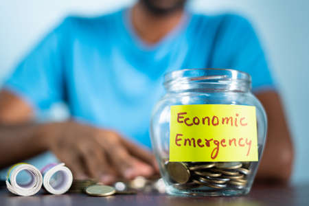 Concept of economic emergency - unrecognizable man counting money by taking out collected coins from jar.の写真素材