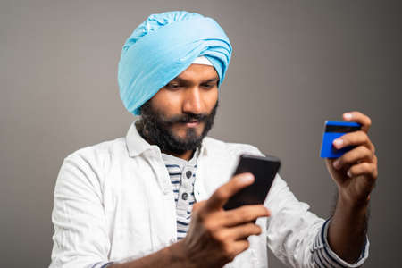 Young sikh man purchasing by paying online using credit card in mobile phone - concept of Online shopping or ordering from e-commerceの写真素材