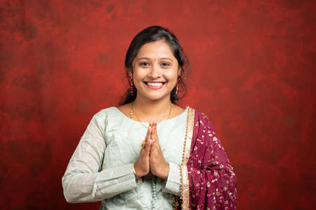 happy smiling Indian girl with traditional ethnic dress in namaste gesture looking at camera - concept of Indian way of greeting.の写真素材