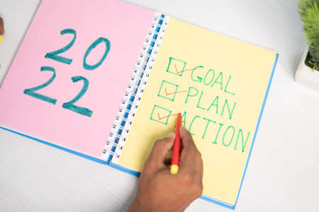 Top view of hands marking 2022 goal, plan and actions on dairy - concept of new year resolution and...