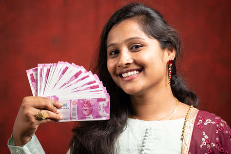 Happy smiling Indian girl using currency notes as fan by looking at camera - concept of Bank credit and loan offers.の写真素材