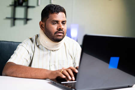 fat man with neck brace working on laptop due to neck pain during work from home - concept of overworking and unhealthy food habits during coronavirus covid-19 pandemicの写真素材