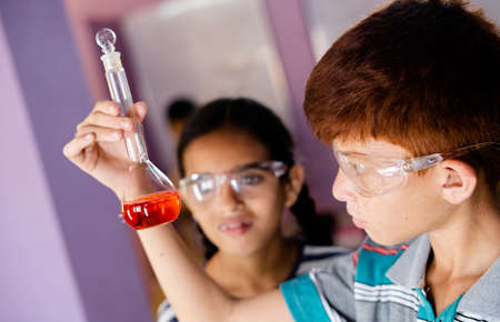 Close up shot of concentrated kid mixing chemicals in Florence flask while making experiment at...