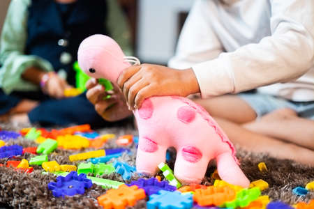 Two unrecognizable little sibling Kids playing with Pink Dinosaur toy at home - concept of children development and childhood fun during holydaysの写真素材