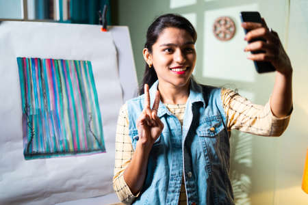 professional woman artist taking selfie in front of her painting with victory or v sign to share on...