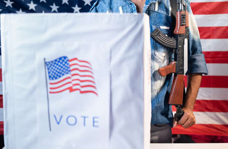 Focus on gun, Concept of US election gun violence, voter fraud and threat at polling station during presidential elections showing with unrecognizable voter with gun at polling booth.の写真素材