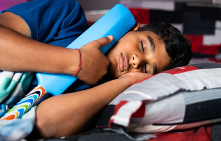Teenager kid sleeping by holding cricket bat - concept of childhood dream of becoming cricketer, player, and objective.の写真素材