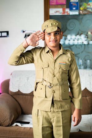 Portrait shot of Kid with police costume saluting by looking camera at home - concept of children...