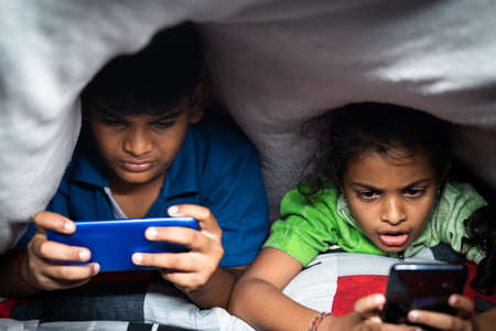 Kids busy playing video game on mobile phone at night under the bedsheet - concept smartphone and technology addiction, unhealthy childhood lifestyleの写真素材