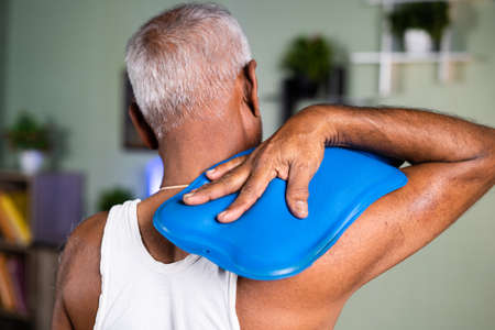 Back view of old man using Hot water bag for neck pain relief - concept of natural hot water therapy...