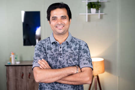 Portrait of smiling Indian handsome young man with crossed arms looking at camera - concept of...