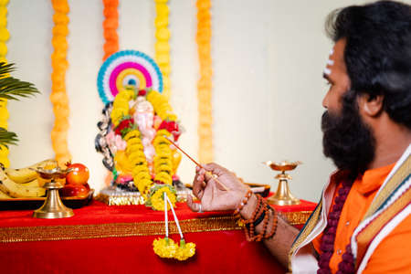 Focus on hand Holy god man or Indian priest offering aarti by chanting hymns in front of lord ganesh...