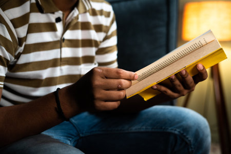 Focus on book unrecognazible young man studying book before going to sleep - concept of novel reading hobby, aspirant and bedtime readingの写真素材