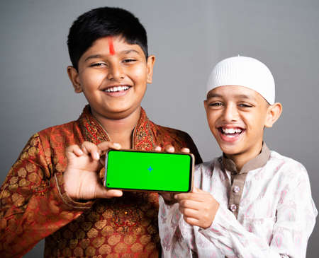 Happy smiling multiethnic Indian religious Kids holding mobile with green screen on gray background - concpet of Application advertisement promotion, friendship and unity in diversity.の写真素材
