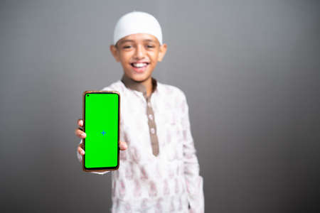 smilling indian muslim kid showing green screen mobile phone by looking at camera - concept of...