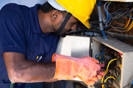Focus on hand, young electrical engineer with protective workware repairing or connecting wires by...