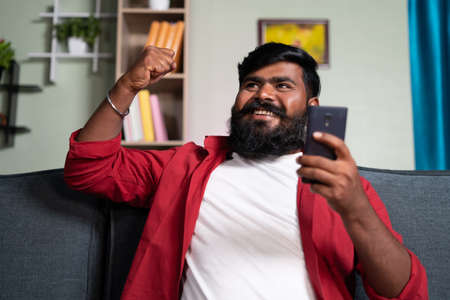 Excited celebrating young man over winning lottery after seeing mobile phone - concept of happiness, got good news or promotion and achievementの写真素材