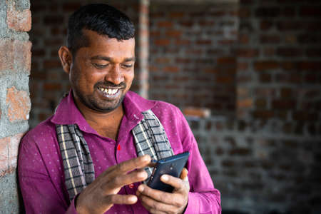 Happy smiling construction worker buys using mobile phone at site showing with copy space - concept...